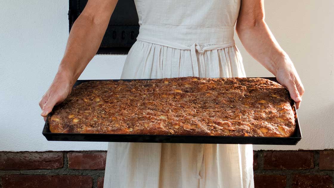 Eine Frau haelt ein Blech mit frisch gebackenem Butterkuchen